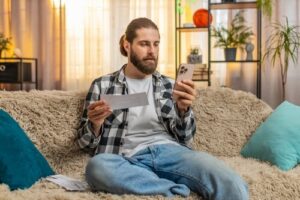 Mann sitzt mit Handy und Rechnung auf dem Sofa.